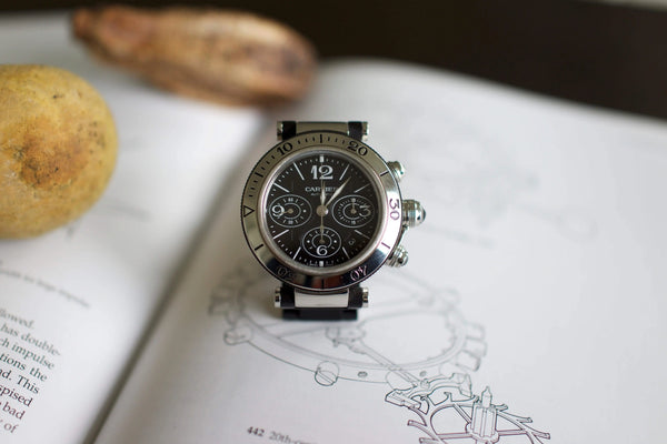Stainless steel chronograph watch with black dial placed on an open book with sketches