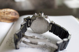 Stainless steel chronograph watch with black bracelet shown from the back on an open book