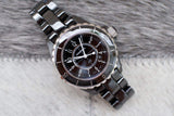 Black ceramic women's luxury watch with round dial and silver bezel on a soft surface