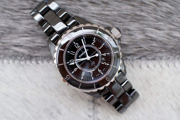 Black ceramic women's luxury watch with round dial and silver bezel on a soft surface