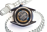 Close-up of luxury watch caseback opened showing battery and movement details, with gear sketch background.