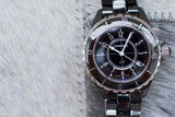 Black ceramic women's luxury watch with silver bezel and black dial on a textured background