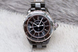 Black ceramic Chanel J12 women's watch with round dial and silver bezel on neutral surface