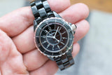 Black ceramic women's luxury wristwatch with round dial and silver bezel held in hand