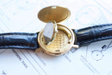 Detailed close-up of an open gold luxury watch case showing the movement and black leather strap.