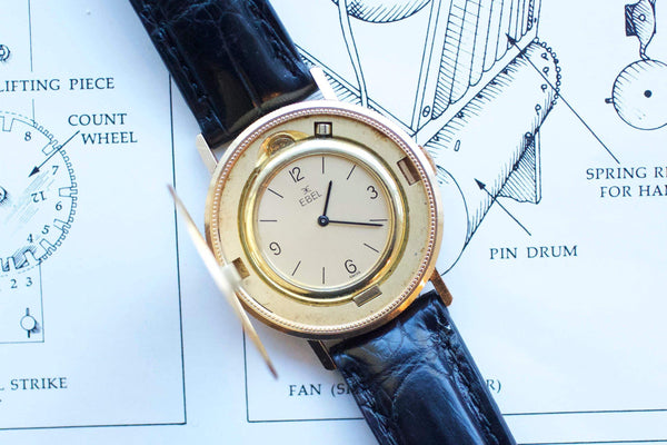 Vintage gold Ebel watch with a black leather strap resting on a technical blueprint.