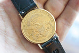 Close-up of a gold twenty dollar coin watch with a black leather strap held in a hand.