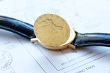 Close-up of a luxury gold watch case back with intricate engravings and a black leather strap.