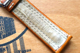 Close-up of a tan leather luxury watch strap with white stitching and embossed branding.