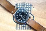 Luxury Swiss-made watch with brown leather strap on a branded wooden surface.