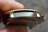 Close-up of a stainless steel luxury watch case with gold-tone bezel and engravings.
