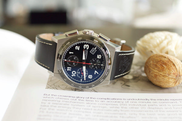 Luxury chronograph watch with black dial and leather strap on a book