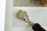 Stainless steel Gucci watch clasp with leather strap on open book, luxury watch detail