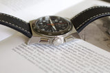 Luxury chronograph watch with black dial and leather strap on open book