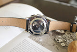 Luxury Swiss chronograph watch with transparent case back and leather strap on an open book