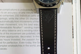 Luxury chronograph watch with black leather strap and white stitching close-up on book
