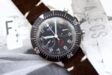 Vintage Heuer Bund SG 1550 flyback chronograph with black dial and brown suede strap.