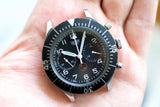 Vintage Heuer Bund Flyback chronograph watch with black dial and subdials, held in hand