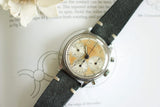 Vintage chronograph wristwatch with patina dial and black leather strap on open book