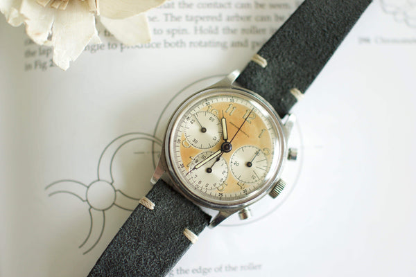 Vintage chronograph wristwatch with patina dial and black leather strap on open book