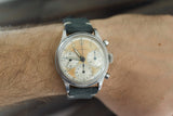 Vintage chronograph wristwatch with cream dial and black leather strap on wrist