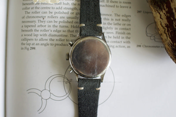 Vintage chronograph watch with a black leather strap, caseback view, on an open book