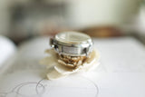 Vintage stainless steel watch case with engraved serial number, placed on a light flower