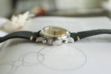 Side view of vintage stainless steel chronograph wristwatch with black leather strap