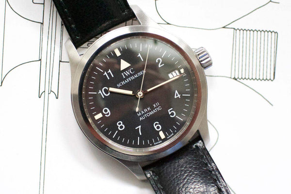 IWC Mark XII automatic men's pilot watch with black dial and leather strap on white schematic background