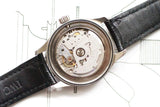 Close-up of a Swiss automatic watch movement with black leather strap on technical drawing background