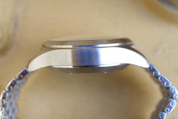 Side view of a stainless steel luxury watch case with a metal bracelet on a light surface