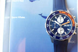 Blue luxury dive chronograph watch with orange accent and rubber strap on a blue background