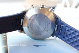 Back view of a luxury Swiss chronograph watch with blue textured rubber strap on a blue surface