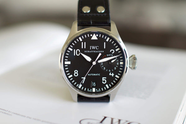 IWC Big Pilot watch with black dial, leather strap, and date display on open book