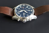 Stainless steel chronograph watch with blue dial and brown leather strap on black background