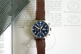Luxury IWC chronograph watch with blue dial and brown leather strap on technical book