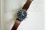 Blue dial chronograph watch with brown leather strap resting on an open book