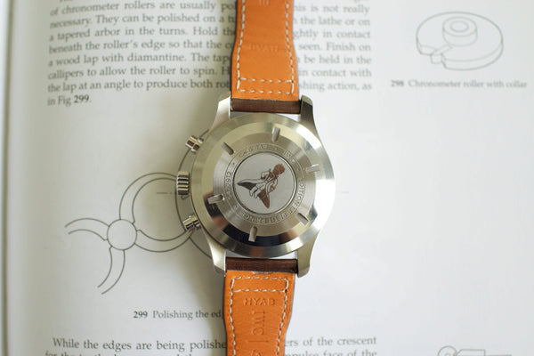 Luxury watch with brown leather strap, engraved case back featuring Le Petit Prince design, on open book.