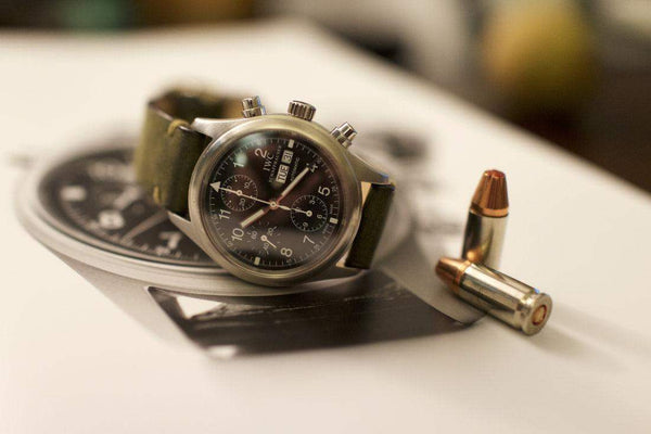 Stainless steel chronograph watch with green leather strap next to two bullets on a magazine