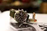 Luxury pilot chronograph watch with black dial and green leather strap, displayed with bullets