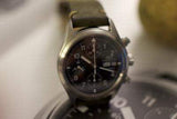 Stainless steel chronograph watch with black dial and leather strap, close-up view.