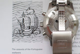 Stainless steel IWC watch caseback with engraved text, next to paper with ship illustration.