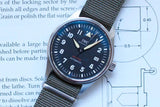 IWC Spitfire Automatic luxury watch with olive green NATO strap on technical blueprints.