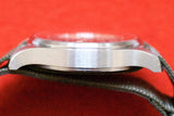Side profile of a luxury Swiss watch with a brushed steel case and leather strap on red background