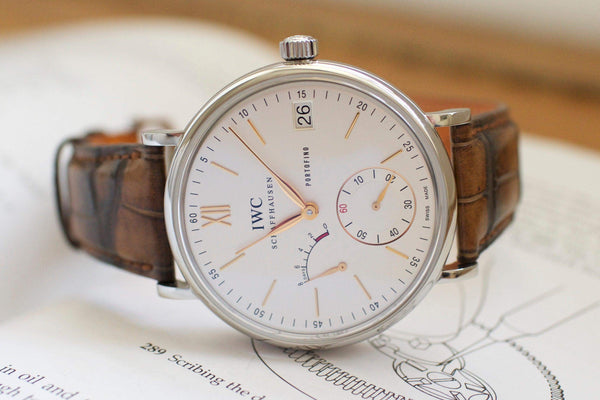 Luxury Swiss watch with white dial, brown leather strap, and gold-tone markers on an open book