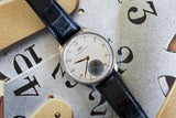Silver luxury wristwatch with black leather strap and gold numerals on artistic clock background