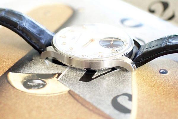 Close-up of a luxury Swiss watch with a silver case and black leather strap on a magazine