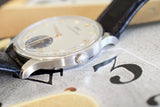 Close-up of a luxury Swiss watch with a silver case, white dial, and black leather strap