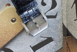 Close-up of a black leather watch strap with IWC clasp on a textured background with numbers.