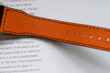 Close-up of orange leather watch strap with visible stitching and embossed text on paper background